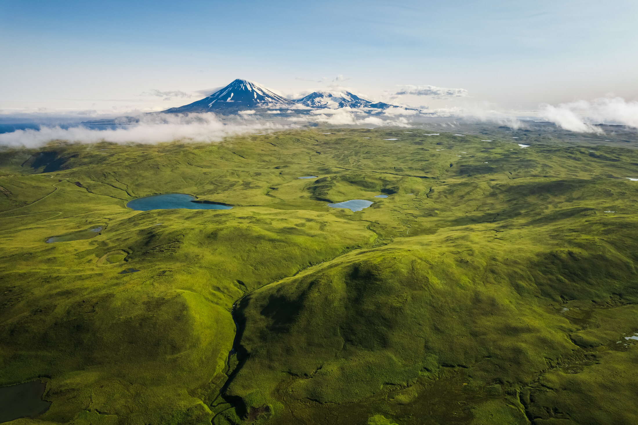 Mount Vsevidof and Mount Recheshnoi rising beyond green grasslands on Umnak Island